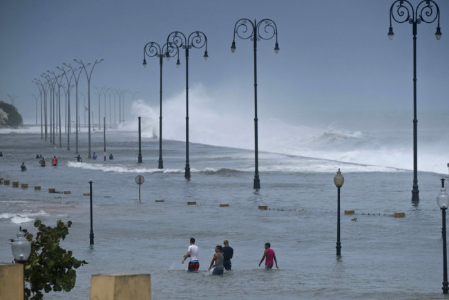 Residents walk on Havana's flooded sea wall as the ocean crashes into it, after the passing of Hurricane Irma in Havana, Cuba, Sunday, Sept. 10, 2017. The powerful storm ripped roofs off houses, collapsed buildings and flooded hundreds of miles of coastline after cutting a trail of destruction across the Caribbean. [Photo: AP/Ramon Espinosa]