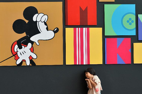 A child plays in front of a wall presenting Disney figure Mickey at the Walt Disney 90th Anniversary Exhibition in Indigo Department Store in Beijing, Sept 6, 2014.[Photo: Xinhua]