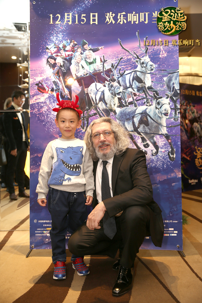 French producer-actor Alain Chabat poses with a young audience member for a picture following the Chinese premiere of his film "Santa & Cie" in Beijing on Dec 11, 2017.[Photo: China Plus]