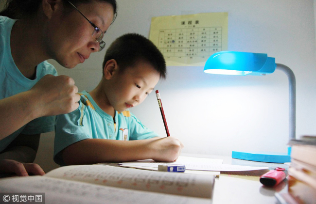 A mother helps her son with his homework. [File photo: VCG]