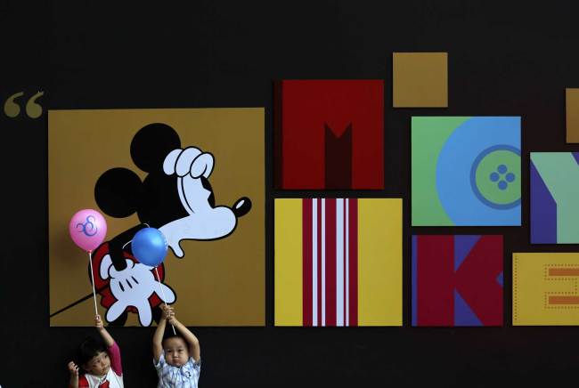 Children play with balloons in front of a huge Mickey Mouse drawing on display at the Disney's 90th Anniversary Exhibition in Beijing, China, Sunday, Sept. 7, 2014. [File photo；AP/Andy Wong]