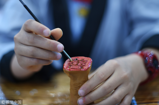 A pupil is carving the Chinese character “kind” on a cube of clay, April 20, 2018. [Photo: VCG]