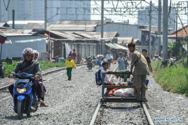 A man pushes an artificial stroller carrying passengers at a railway track at Kampung Bandan in North Jakarta, Indonesia, Sept. 8, 2015.[Photo: Xinhua]