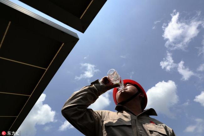 A worker drinks bottled water to quench his thirst at a solar power station in Chongqing, July 27, 2018. The municipality has been gripped with temperatures hitting above 40 degrees through July. [Photo: IC]