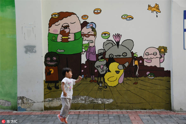 A child jumps in front of a street mural in Guiyang city, Southwest China's Guizhou province, July 29, 2018. [Photo/IC]