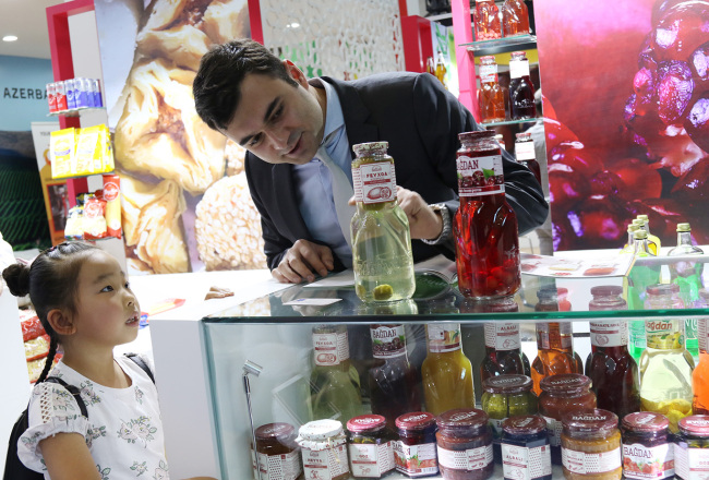 An Azerbaijani exhibitor introduces his company's compotes, a unique local food, to a visiting child during the 6th China-Eurasia Expo in Urumqi, Xinjiang Uygur Autonomous Region on Thursday, August 30, 2018. [Photo: China Plus / Sang Yarong]