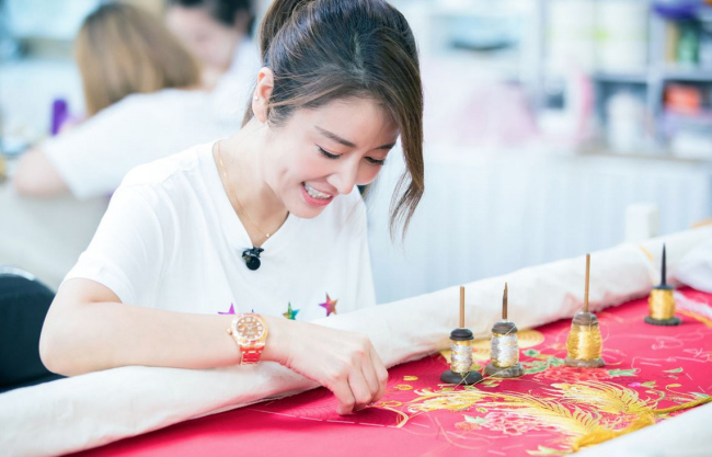 Taiwan Actress Ruby Lin tries embroidery during a publicity event for an auspicious wedding dress made by master couturier Guo Pei. [Photo: provided to China Plus]