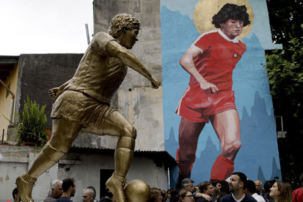 People stand beside statue of Diego Maradona soccer star during its presentation in Buenos Aires, Argentina, Wednesday, October 31, 2018. The statue by artist Jorge Martinez, was presented Wednesday to honor Maradona on his 58th birthday Tuesday, next to the stadium of the Buenos Aires based club where the Argentine soccer great began his career. [Photo: Imagine China]