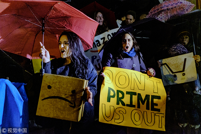 Demonstrators hold placards and cardboard boxes featuring an altered version of the Amazon.com Inc. logo during a protest against the planned Amazon office hub in the Long Island City neighborhood in the Queens borough of New York, U.S., on Monday, Nov. 26, 2018. [Photo: Bloomberg via Getty Images/Christopher Lee]