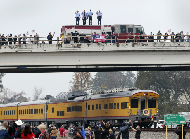 Firefighters stand on their truck and salute along with other attendants on an overpass as the train carrying the body of former president George H.W. Bush travels past on the way to Bush's final internment Thursday, Dec. 6, 2018, in Spring, Texas. [Photo: AP/Michael Wyke]
