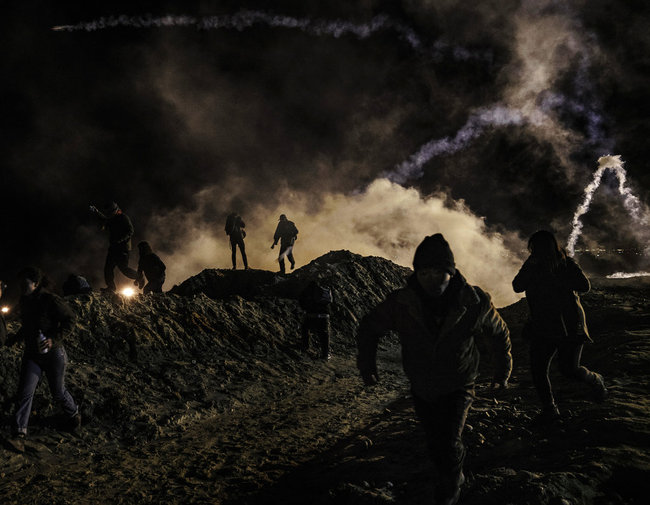 Migrants run as tear gas is thrown by U.S. Border Protection officers to the Mexican side of the border fence after they climbed the fence to get to San Diego, Calif., from Tijuana, Mexico, Tuesday, Jan. 1, 2019. Discouraged by the long wait to apply for asylum through official ports of entry, many migrants from recent caravans are choosing to cross the U.S. border wall and hand themselves in to border patrol agents. [Photo: AP]