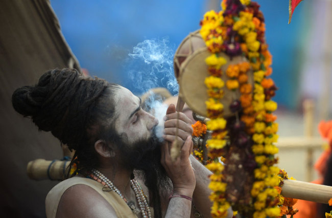 An Indian Hindu Sadhu (holy man) sits outside his tent as he smokes ahead of the Kumbh Mela festival in Allahabad on January 13, 2019. [Photo: AFP/SANJAY KANOJIA]