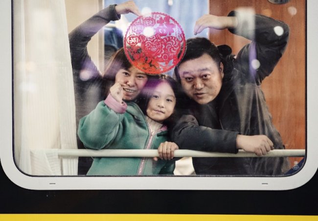 A girl and her parents pose for a photo behind a "Lucky Character" window on a train at the Beijing Railway Station on Monday, January 21, 2019. [Photo: China Plus/Li Jin]