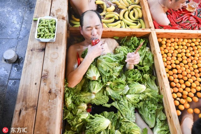 A man enjoys(享受 xiǎngshòu) drinks and kebabs amongst lettuce in the nine-grid hotpot-shaped hot spring pool filled with vegetables and fruits at a hotel in Hangzhou, east China's Zhejiang Province, January 27, 2019. [Photo: IC]