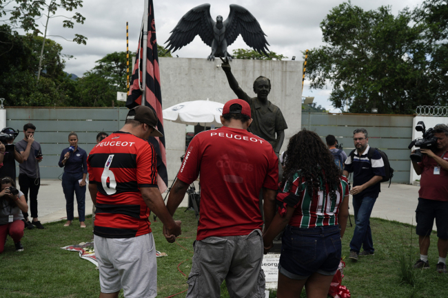 Fans hold hands as they pray in a homage to the victims of a fire at the Flamengo soccer club training complex in Rio de Janeiro, Brazil, Friday, Feb. 8, 2019. A fire tore through the sleeping quarters of the Flamengo soccer club development league, one of Brazil's most popular professional soccer clubs, killing several people who were most likely players and injuring others, authorities said. [Photo: AP/Leo Correa]