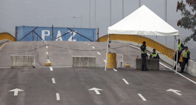 Colombian police stand on the Colombian side of the Tienditas International Bridge, which is blocked with a cargo trailer, a fuel tanker and fencing, placed by Venezuelan authorities to block humanitarian aid from entering, on the outskirts of Cucuta, Colombia, on the border with Venezuela, Monday, Feb. 18, 2019. [Photo: AP]
