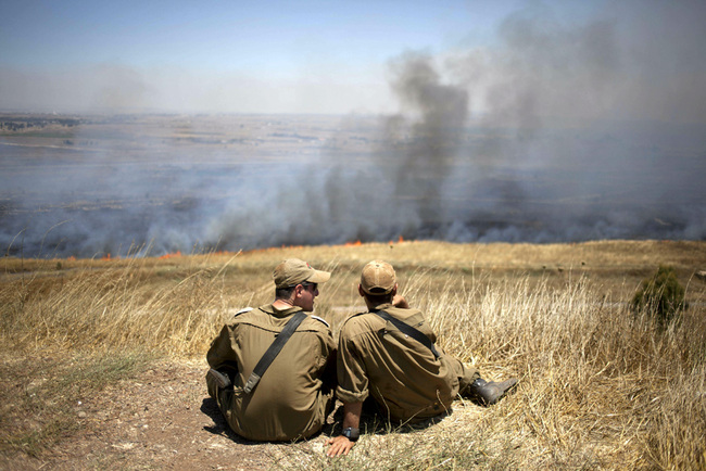 Israeli soldiers sit in a position on the border with Syria on the Golan Heights as smoke rises following explosions of mortar shells, July 16, 2013. [File photo: AP/Ariel Schalit]