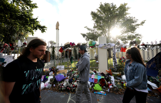 People walk past flowers and tributes displayed in memory of the twin mosque massacre victims outside the Al Noor mosque in Christchurch on March 29, 2019. [Photo: AFP]