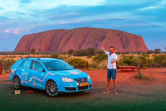 This handout photo taken on December 31, 2018 and released on April 7, 2019 from Dutch driver Wiebe Wakker (C-R) shows him at Uluru in the Northern Territory with his retrofitted station wagon nicknamed "The Blue Bandit" during his round-the-world trip in the electric car. [Photo: PLUG ME IN PROJECT/Wiebe Wakke/AFP]
