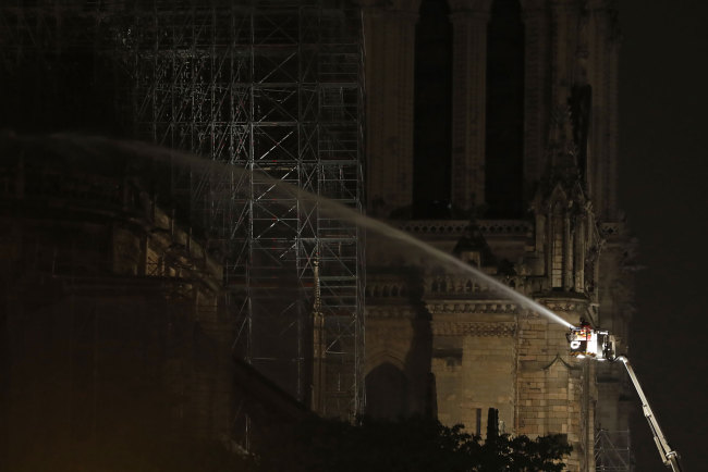A firefighter is seen dousing the facade of the Notre-Dame Cathedral in Paris early on April 16, 2019. [Photo: AFP/Zakaria ABDELKAFI]