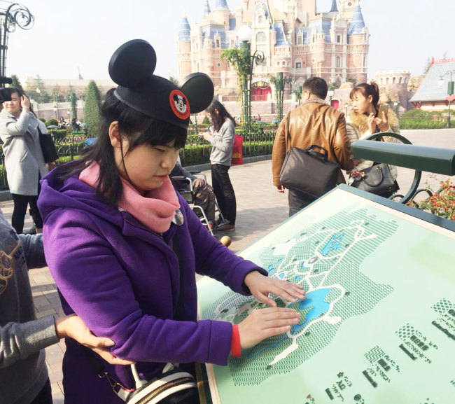 A visually impaired woman uses a braille map at Shanghai Disney Resort. [File photo: Shanghai Observer]
