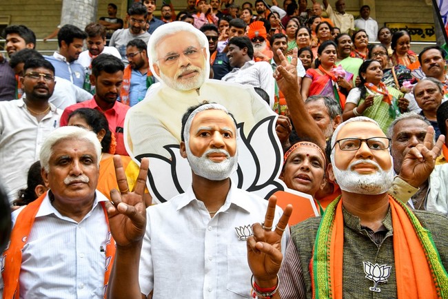 Indian supporters and party workers of Bharatiya Janata Party (BJP) wear masks of Indian Prime Minister Narendra Modi and flash victory signs as they celebrate on the vote results day for India's general election in Bangalore on May 23, 2019. [Photo: AFP]