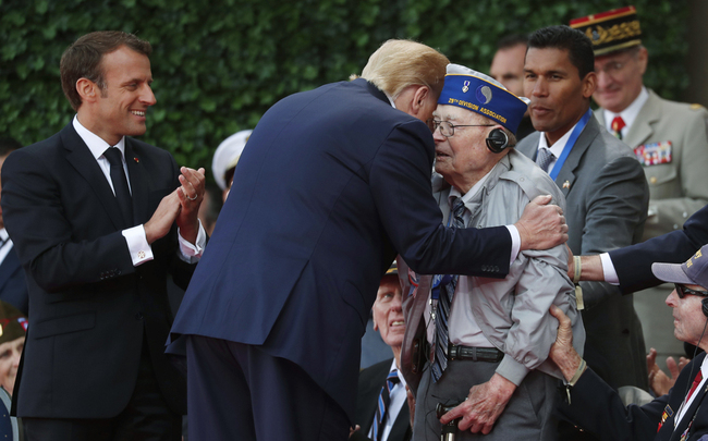 French President Emmanuel Macron (L) applauds as US President Donald Trump (C) greets a US veteran during a French-US ceremony at the Normandy American Cemetery and Memorial in Colleville-sur-Mer, Normandy, northwestern France, on June 6, 2019, as part of D-Day commemorations marking the 75th anniversary of the World War II Allied landings in Normandy. [Photo: Pool/AFP/Ian Langsdon]