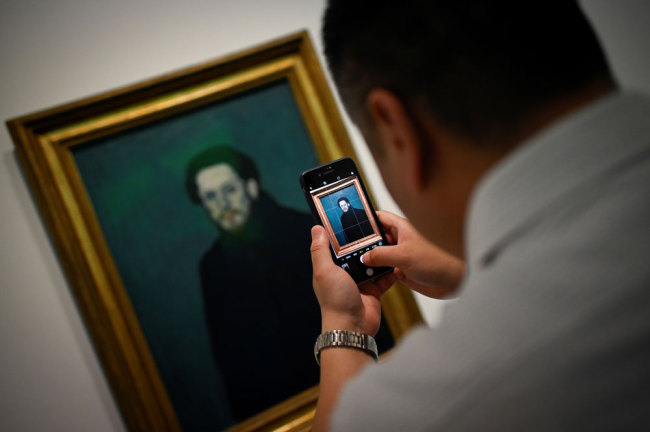 This picture taken on June 14, 2019 shows a man using his mobile phone to take a picture of an oil canvas entitled "Self Portrait" by Pablo Picasso during an exhibition "Picasso Birth of a Genius" at an art gallery in Beijing. [Photo: AFP/Wang Zhao]