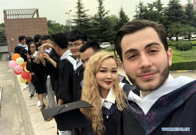 Aushev Djamaleil (R) takes a selfie with his schoolmates in academic dress in Shaanxi University of Chinese Medicine in northwest China's Shaanxi Province.[Photo: Xinhua] 