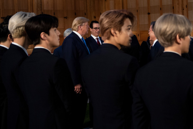 Members of K-pop band EXO (foreground) stand while US President Donald Trump and US Secretary of the Treasury Steven Mnuchin (background, centre L and R), and South Korea's President Moon Jae-in wait for a working dinner at the tea house on the grounds of the presidential Blue House in Seoul on June 29, 2019. [Photo: AFP]