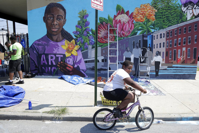 A boy rides his bicycle Monday, July 29. 2019 after volunteering to paint a mural outside the New Song Community Church in the Sandtown section of Baltimore. [Photo: AP]