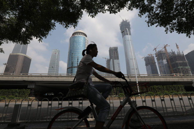 A woman rides a bicycle in central business district (CBD) of Beijing, China, August 14, 2017. [File photo: IC]