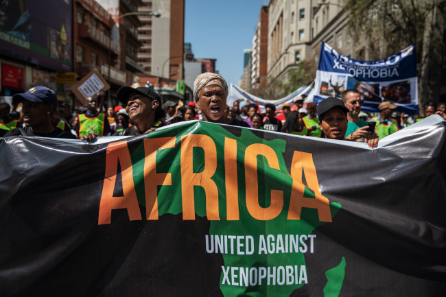 A woman sings as she holds a banner during a civil society groups march against the recent rise of xenophobic attacks in South Africa, on September 14, 2019, in Johannesburg’s Central Business District. [Photo: AFP]