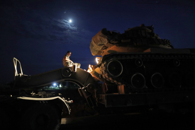 A Turkish army officer prepares to upload a tank from a truck to its new position on the Turkish side of the border between Turkey and Syria, in Sanliurfa province, southeastern Turkey, Tuesday, Oct. 8, 2019. [Photo: AP/Lefteris Pitarakis]