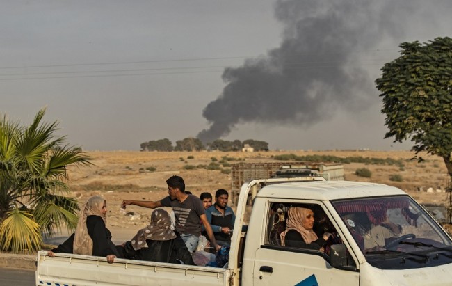 Civilians ride a pickup truck as smoke billows following Turkish bombardment on Syria's northeastern town of Ras al-Ain in the Hasakeh province along the Turkish border on October 9, 2019. [Photo: AFP/Delil Souleiman]