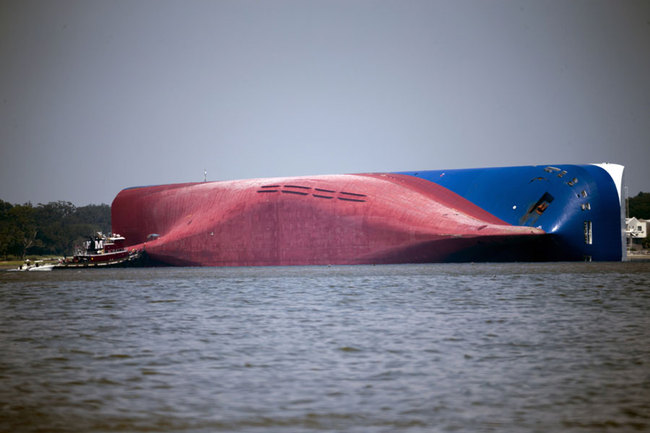 In this Sept. 9, 2019, file photo, a Moran tugboat nears the stern of the capsizing vessel Golden Ray as a tent and rescuers can be seen near the bottom of the ship near the tug boat in Jekyll Island, Ga. Marine salvage experts seeking to remove the overturned cargo ship close to Georgia's seacoast will haul it away in pieces because it cannot be safely righted and refloated intact, their Unified Command said in a statement Saturday, Oct. 12. [Photo: AP/Stephen B. Morton]