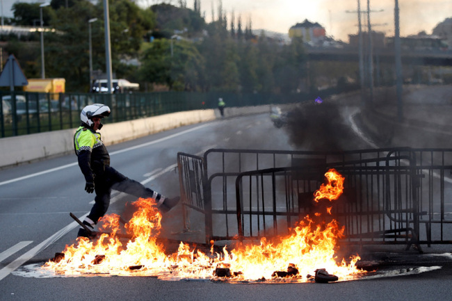 A policeman tries to extinguish a barricade on fire on a highway in Barcelona, Spain, October 18, 2019. [Photo: IC]
