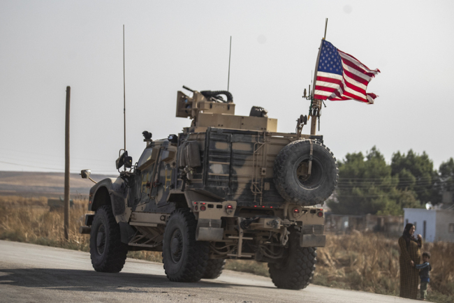 A Syrian woman and a child stand on the side of a road as a US military vehicle drives on a road after US forces pulled out of their base in the Northern Syriain town of Tal Tamr, on October 20, 2019. [Photo: AFP/Delil Souleiman]