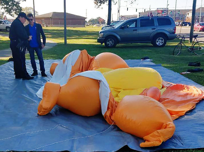 A responding officer and an unidentified man stands by a Baby Trump balloon deflated by someone at Monnish Park as people were protesting President Donald Trump's visit to an NCAA college football game between Louisiana State and Alabama playing nearby in Tuscaloosa, Ala., Saturday, Nov. 9, 2019. [Photo: AP]