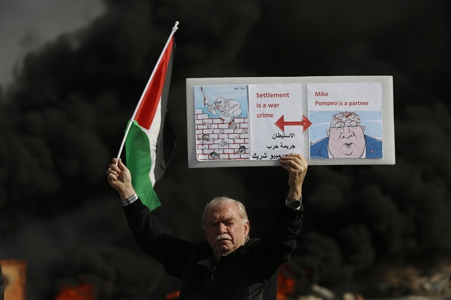 Palestinian hold poster depicting Israeli Prime Minister Benjamin Netanyahu, left, and US Secretary of State Mike Pompeo as clashes with Israeli troops broke out during the protest against the U.S. announcement that it no longer believes Israeli settlements violate international law., at checkpoint Beit El near the West Bank city of Ramallah, Tuesday, Nov. 26, 2019. [Photo: AP/Majdi Mohammed]