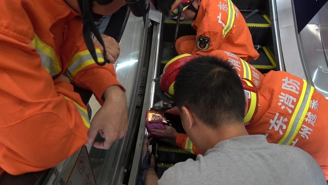 Firefighters use a grinder to cut open an escalator to release the trapped foot of a boy in the city of Guangzhou, Guangdong Province, on Sunday, December 1, 2019. [Photo: VCG]