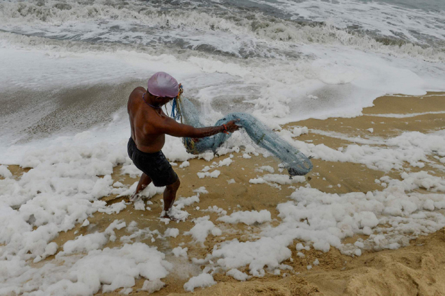 A fisherman retrieves fish from his net as foamy discharge, caused by pollutants, mixes with surf on a beach in Chennai on December 02, 2019. [Photo: VCG]