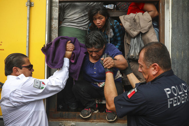 In this Nov. 26, 2019 photo, a federal police officer assigned to the National Guard and a migration agent help a woman off the cargo hold of a truck packed with migrants being smuggled, at an immigration checkpoint where the truck was stopped in Medellín de Bravo, Veracruz state, Mexico. [Photo: AP]