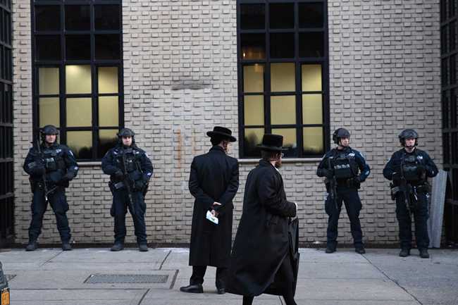 File Photo: Orthodox Jewish men pass New York City police guarding a Brooklyn synagogue prior to a funeral for Mosche Deutsch in New York on Dec. 11, 2019.[Photo: AP/Mark Lennihan]