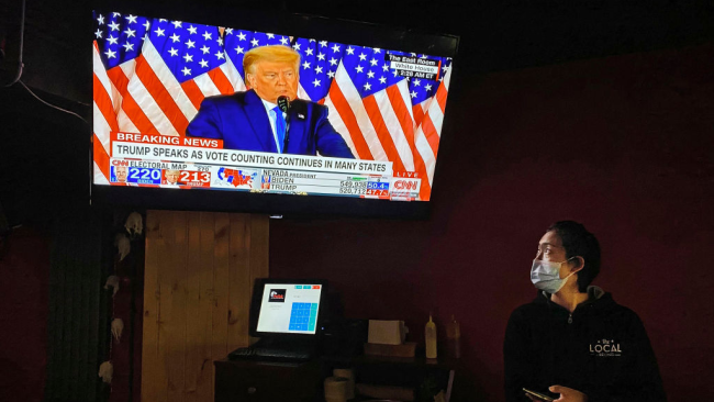 Servírka s ochrannou maskou při sledování projevu amerického prezidenta Donalda Trumpa v televizi během akce sledující volby v místním baru v čínském Pekingu, 4. listopadu 2020. / Getty Images