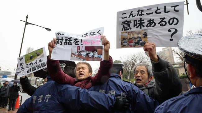 Demonstranti nesou nápisy, když policisté tvoří kordon během cvičení raketového útoku v Tokiu v Japonsku 22. ledna 2018. / CFP
