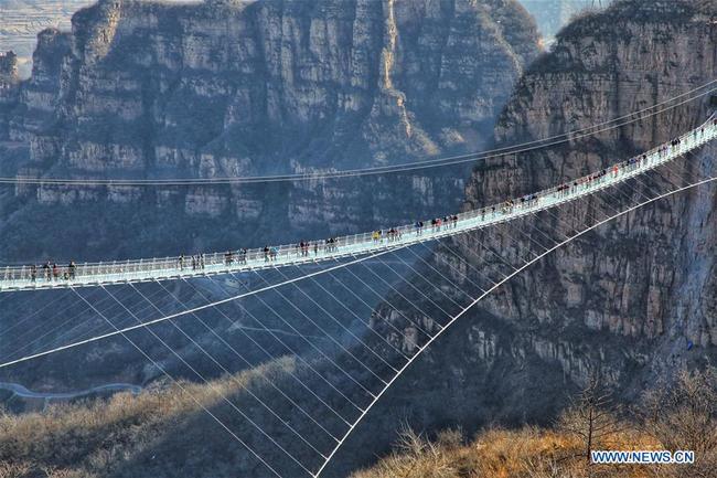 Des touristes marchent sur un pont suspendu en verre dans le site touristique de Hongyagu à Pingshan, district de la province chinoise du Hebei (nord), le 24 décembre 2017. Le pont suspendu en verre, d'une longueur de 488 mètres, a officiellement ouvert au public dimanche. (Xinhua/Liu Peiran)