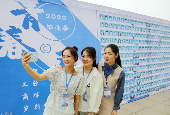 Απόφοιτες της Επαγγελματικής Σχολής Επιστήμης και Τεχνολογίας του Ναντόνγκ, της επαρχίας Τζιανγκσού της Ανατολικής Κίνας ποζάρουν μια φωτογραφία μπροστά από έναν πίνακα των αποφοίτων της χρονιάς, 16 Μαΐου. (Φωτογραφία/ People’s Daily Online)