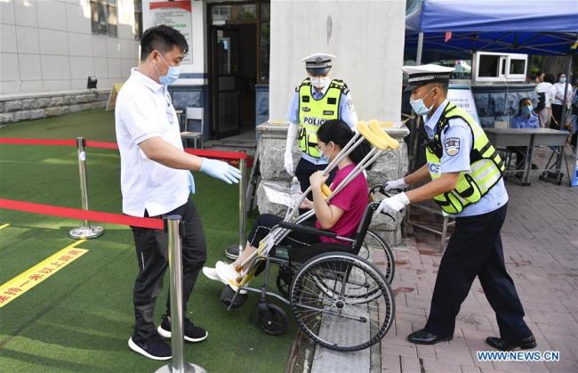 Ένα μέλος του προσωπικού βοηθά μια εξεταζόμενη με ειδικές ανάγκες να εισέλθει στον χώρο των εξετάσεων σε ένα λύκειο στο Τσανγκτσούν, πρωτεύουσα της επαρχίας Τζιλίν της ΒΑ Κίνας, στις 7 Ιουλίου 2020.(Xinhua / Xu Chang)<br>