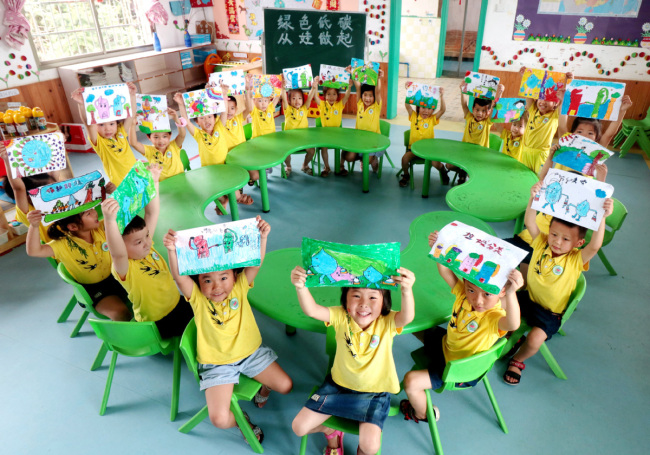 Τα παιδιά σε ένα νηπιαγωγείο στην πόλη Λιανγιουάν της επαρχία Χουνάν, Νότιας Κίνας, παρουσιάζουν τους πίνακες τους υποστηρίζοντας τον τρόπο ζωής χαμηλών εκπομπών διοξειδίου του άνθρακα στις 2 Ιουλίου 2020. [Φωτογραφία / Xinhua]